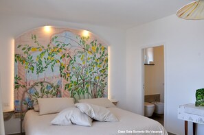 Ein Schlafzimmer mit Wandgemälde eines Baumes und Blumen, einem Bett mit Kissen und einem kleinen Tisch mit einem Korb.