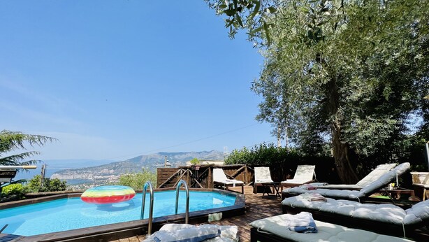 Una terraza de madera con piscina, sillas de descanso y vistas al mar y a las montañas.