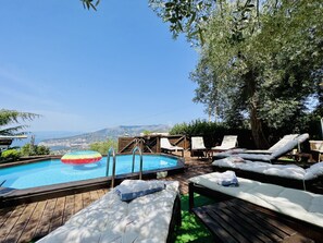 Eine Holzterrasse mit Pool, Liegestühlen und Blick auf das Meer und die Berge.