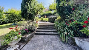 Una escalera de piedra conduce a una casa, rodeada de jardines cuidados y diversas plantas.
