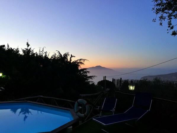 Ein Poolbereich mit Liegestühlen und einem Rettungsring mit Blick auf eine Berglandschaft bei Sonnenuntergang.