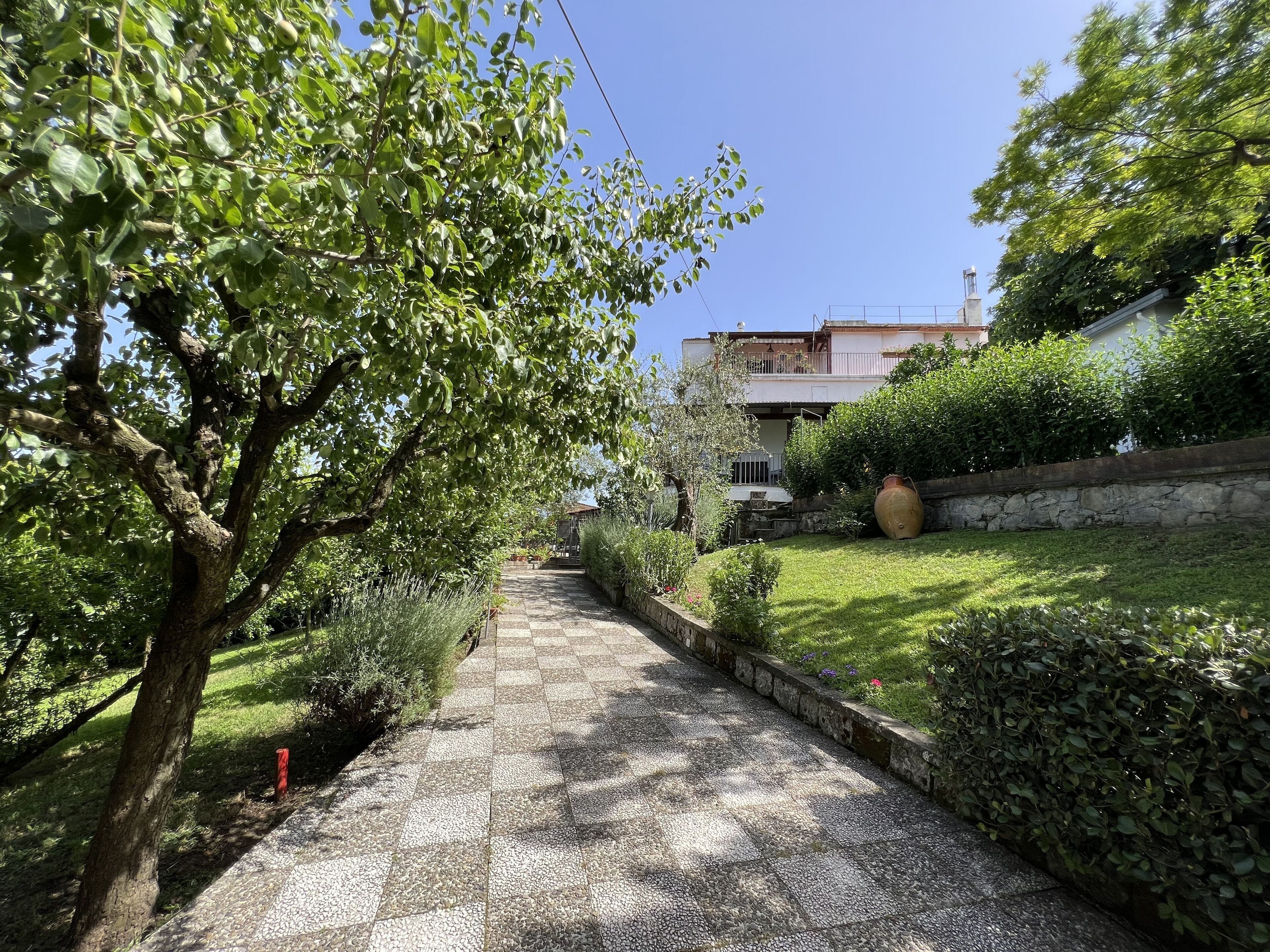 Un chemin pavé mène à un bâtiment doté d’un mur en pierre et agrémenté de verdure.