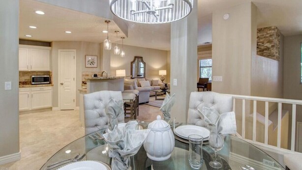 A spacious living area with a glass dining table set for four, a chandelier, and a view of the kitchen and living room. - Luxury Living in Kierland Greens (Scottsdale)