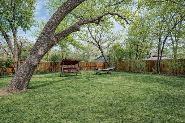 A backyard with a swing set, a hammock, and a wooden fence.