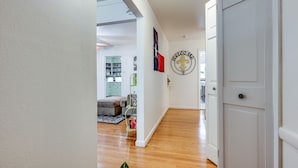 A hallway with a wooden floor, white walls, and a closed door. There is a 'WELCOME' sign on the wall. - Cheerful Home W/ Private 15' Swim Spa, Big Fenced Yard, & Fire Pit (Arlington)