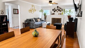 A living room with a sofa, a dining table with chairs, a fireplace, and a ceiling fan. - Cheerful Home W/ Private 15' Swim Spa, Big Fenced Yard, & Fire Pit (Arlington)