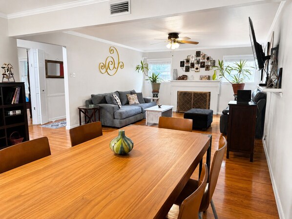 A living room with a sofa, a dining table with chairs, a fireplace, and a ceiling fan.