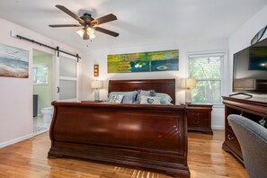 A bedroom with a wooden bed, a ceiling fan, a painting, a television, and a window with blinds. - Cheerful Home W/ Private 15' Swim Spa, Big Fenced Yard, & Fire Pit (Arlington)