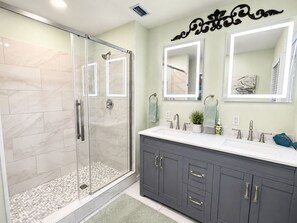 Une salle de bain moderne avec une douche à parois de verre, un meuble-lavabo doté d’un grand miroir et un sol carrelé.