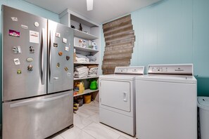 A kitchen with a stainless steel refrigerator, a built-in oven, a washing machine, and a wooden wall panel.