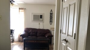 Un couloir mène à un salon où se trouvent un canapé en cuir marron et une table basse en bois foncé.