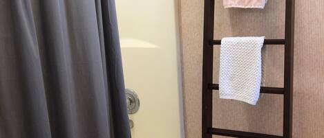 A bathroom with a bathtub, a shower curtain, and a wooden towel rack holding two towels.