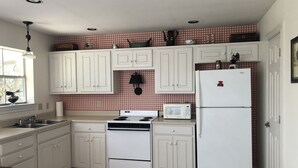 Une cuisine avec des meubles blancs, une cuisinière, un four à micro-ondes et un réfrigérateur.