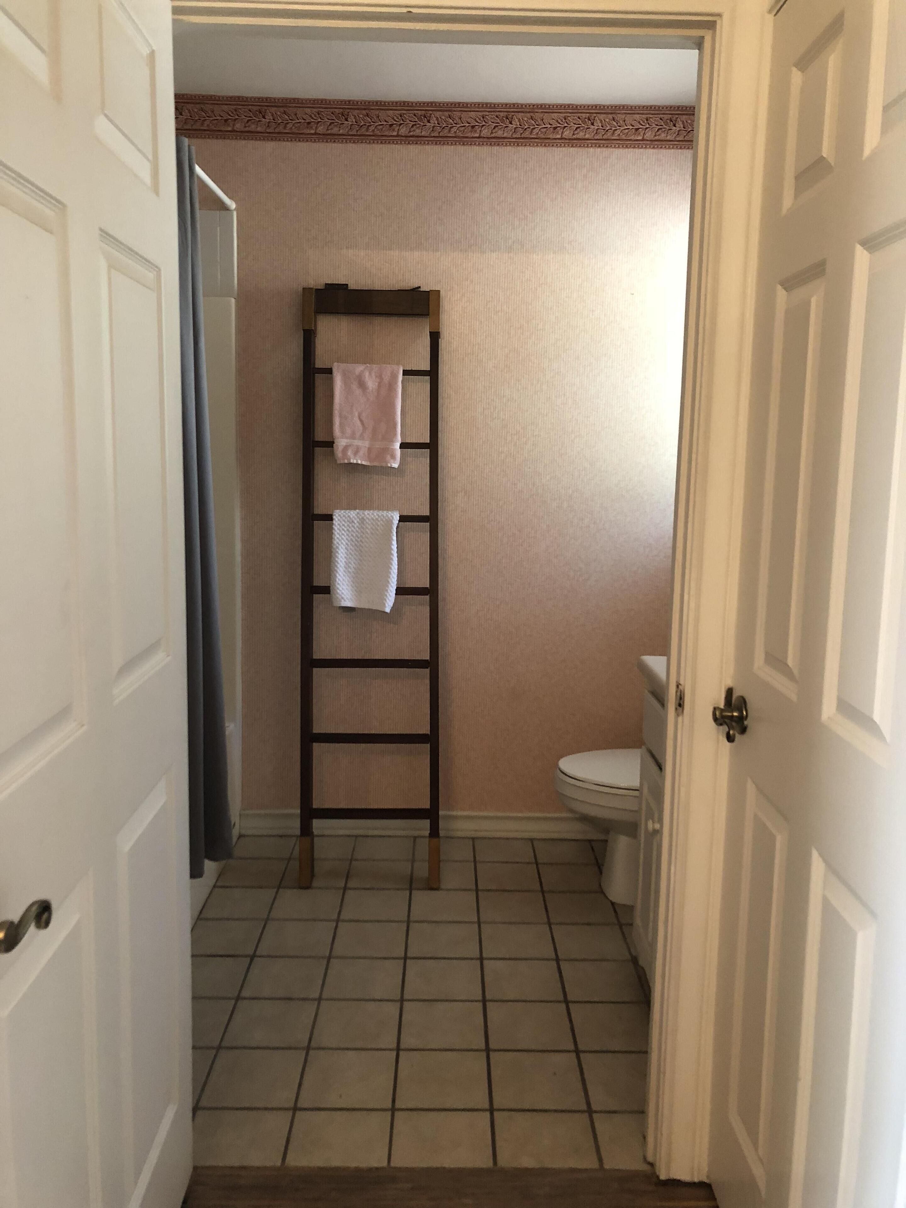 A bathroom with a wooden ladder, two towels, and a toilet.