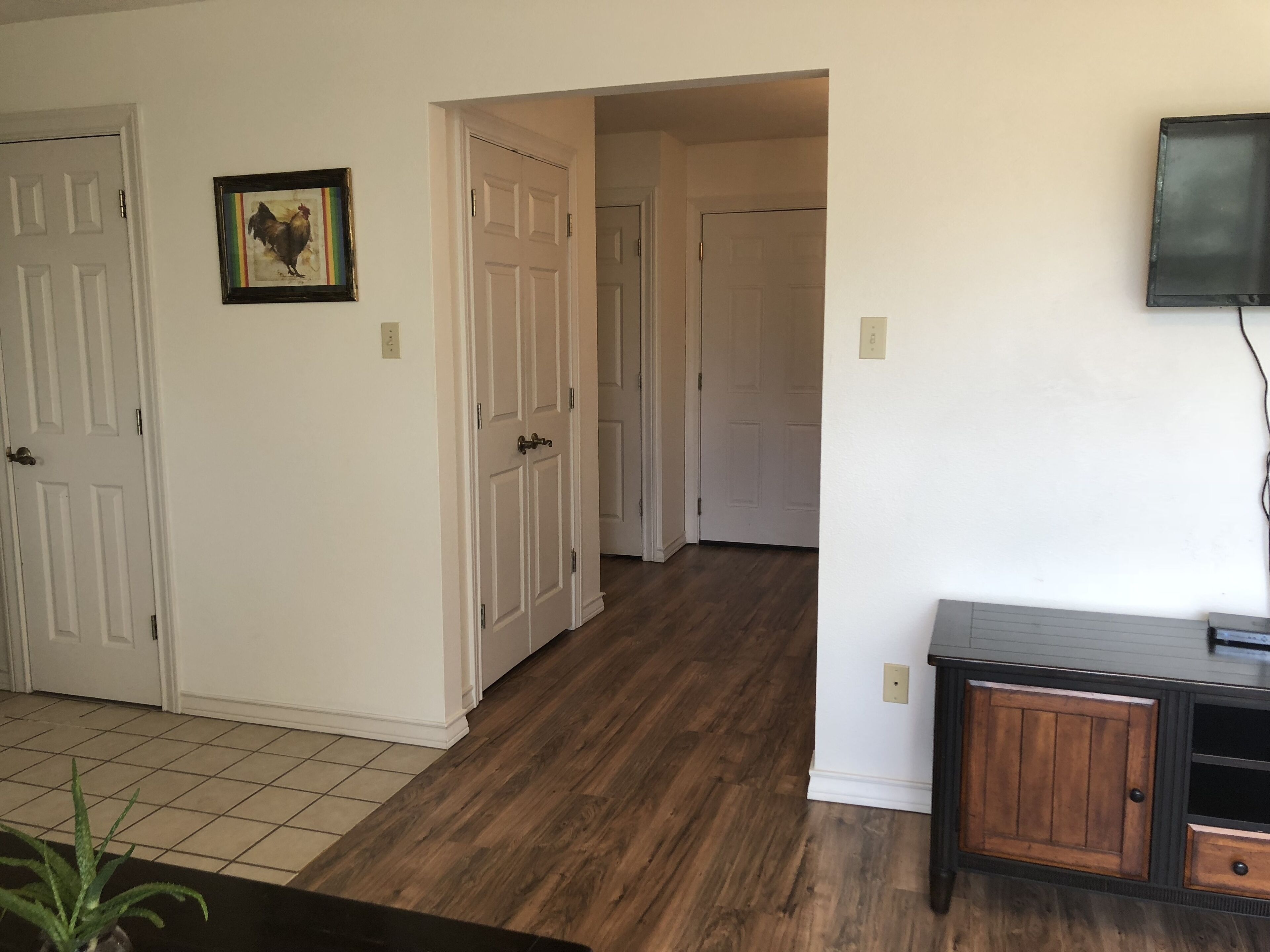 A hallway with wooden flooring, white walls, and a door leading to another room.