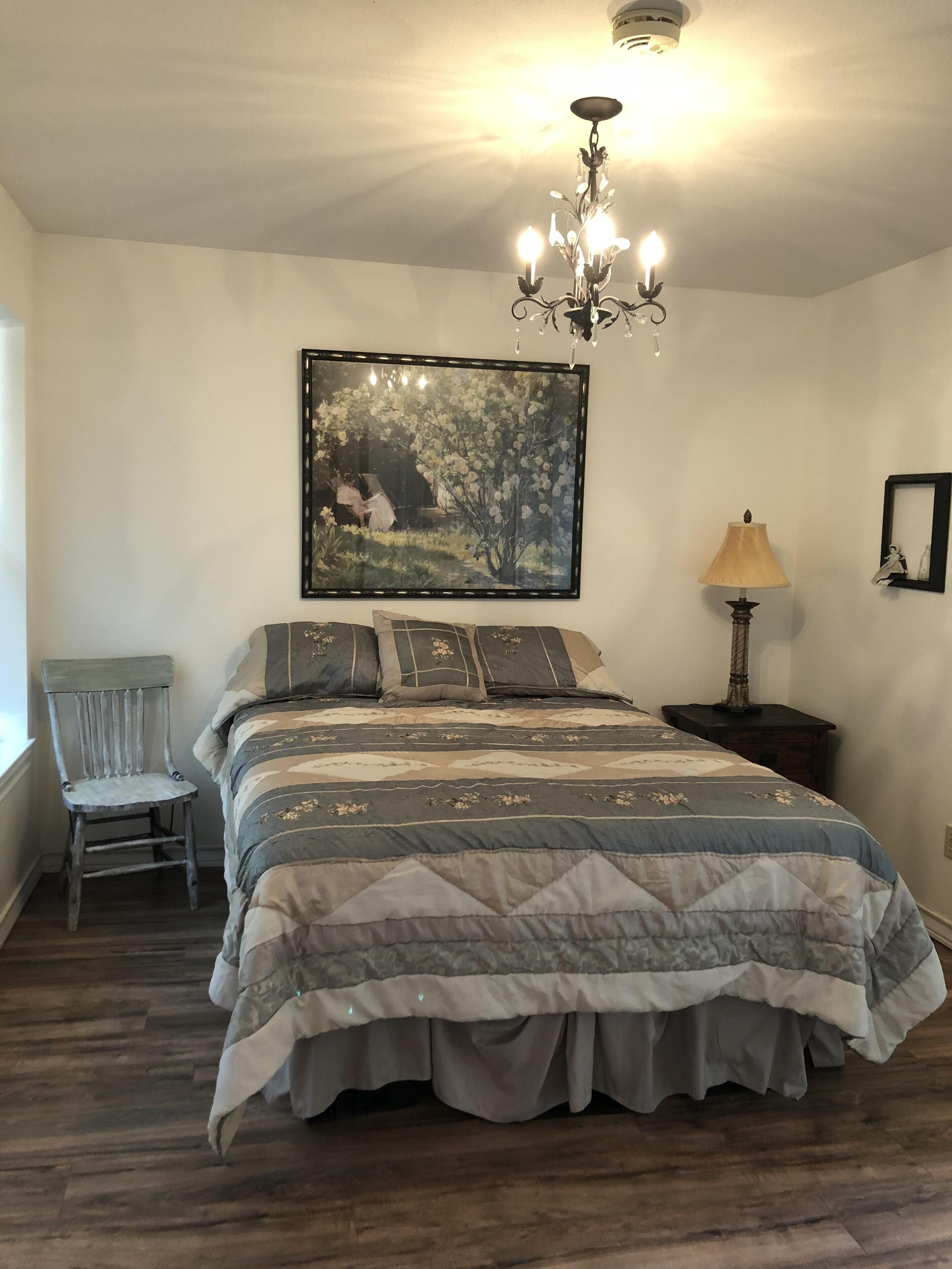 A bedroom with a large bed, a chair, a lamp, and a painting on the wall.