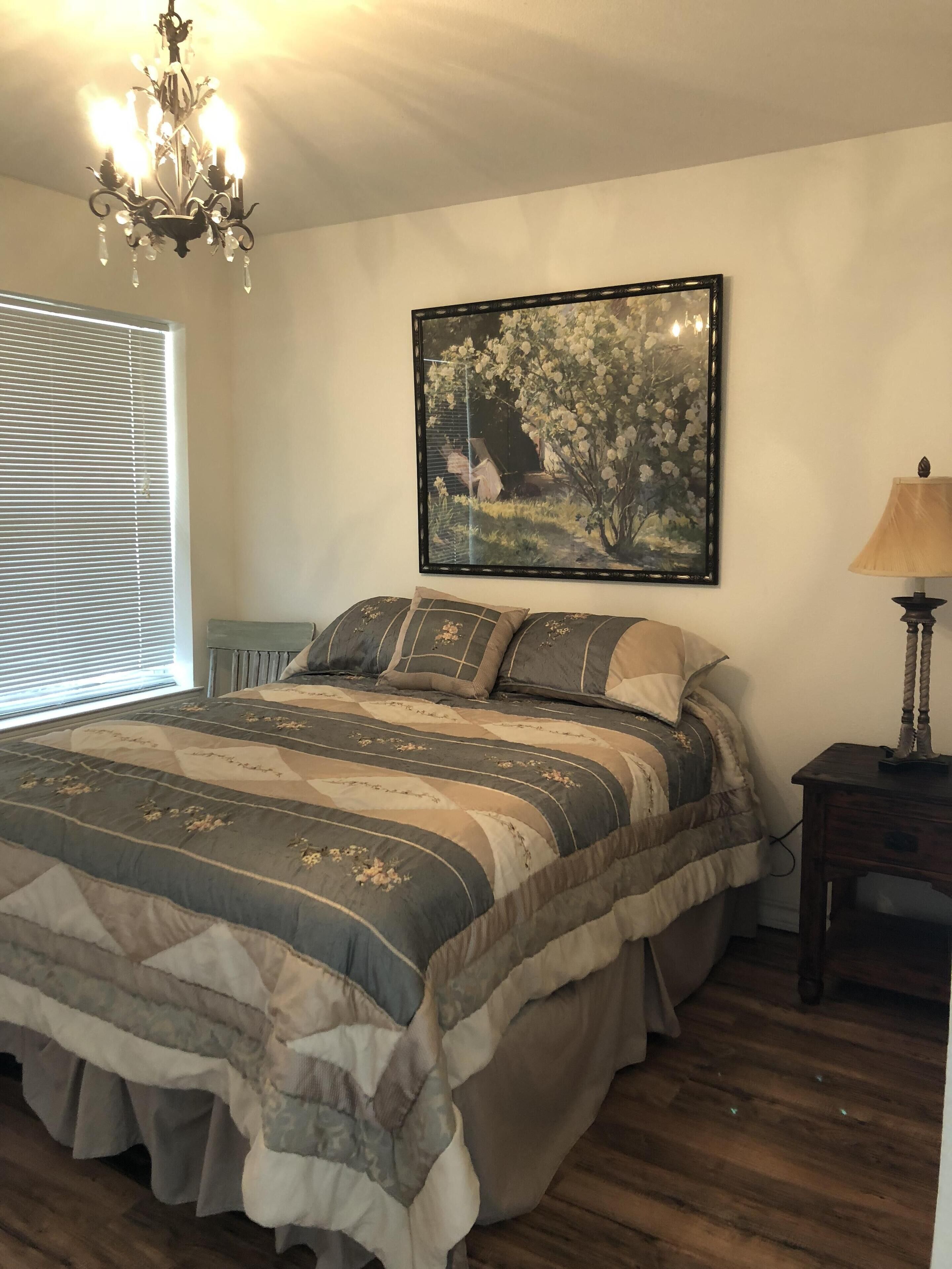 A bedroom with a bed, a chandelier, a painting, and a lamp.