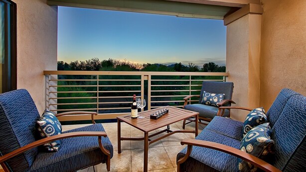 Ein Balkon mit Holztisch, zwei stufenartigen blauen Stühlen und einer Weinflasche.