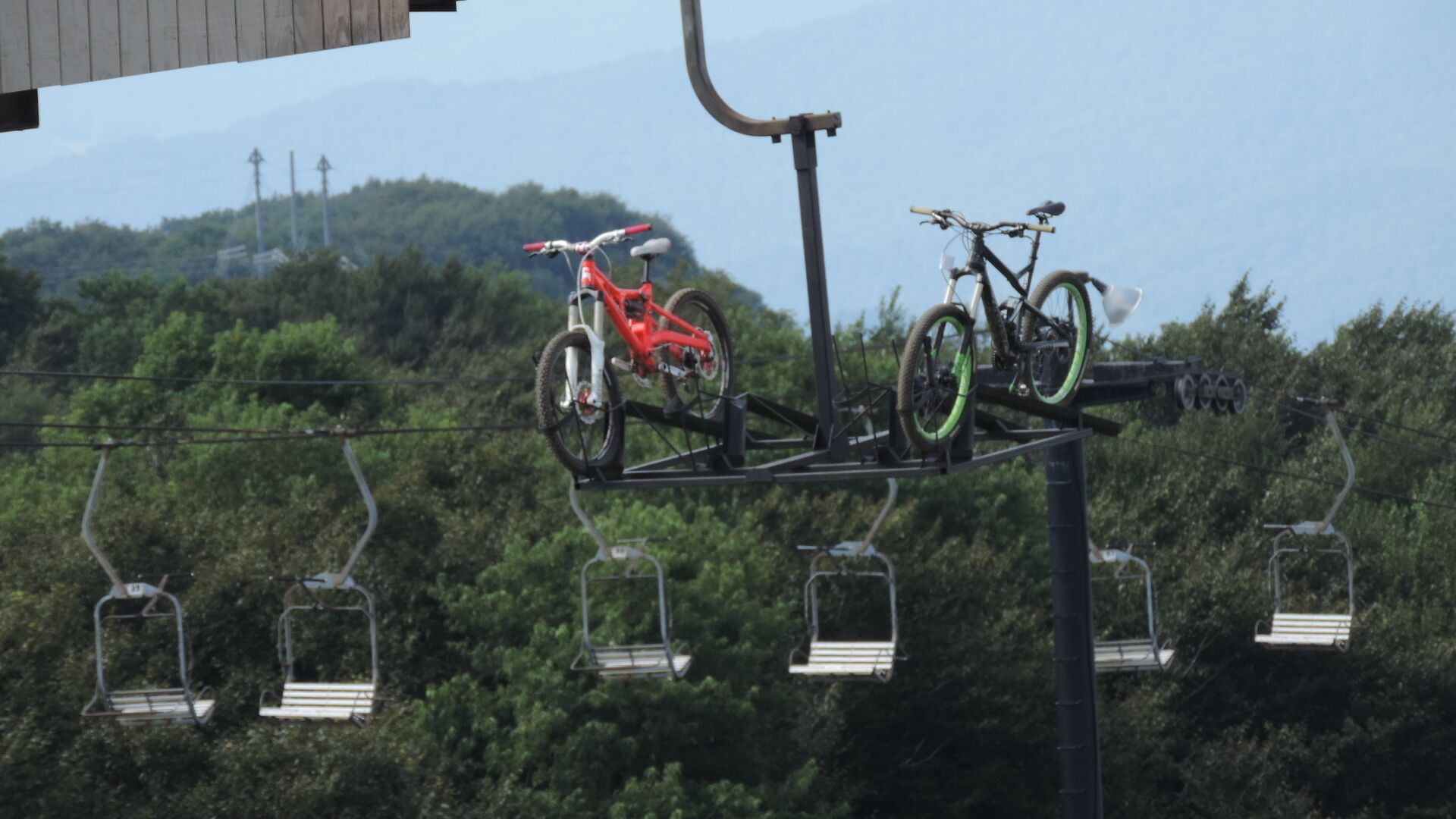 Una bicicleta de montaña sobre un soporte suspendido con un telesilla al fondo.