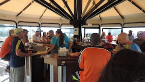 Uma área interna de bar com balcão, banquetas e diversas garrafas nas prateleiras.