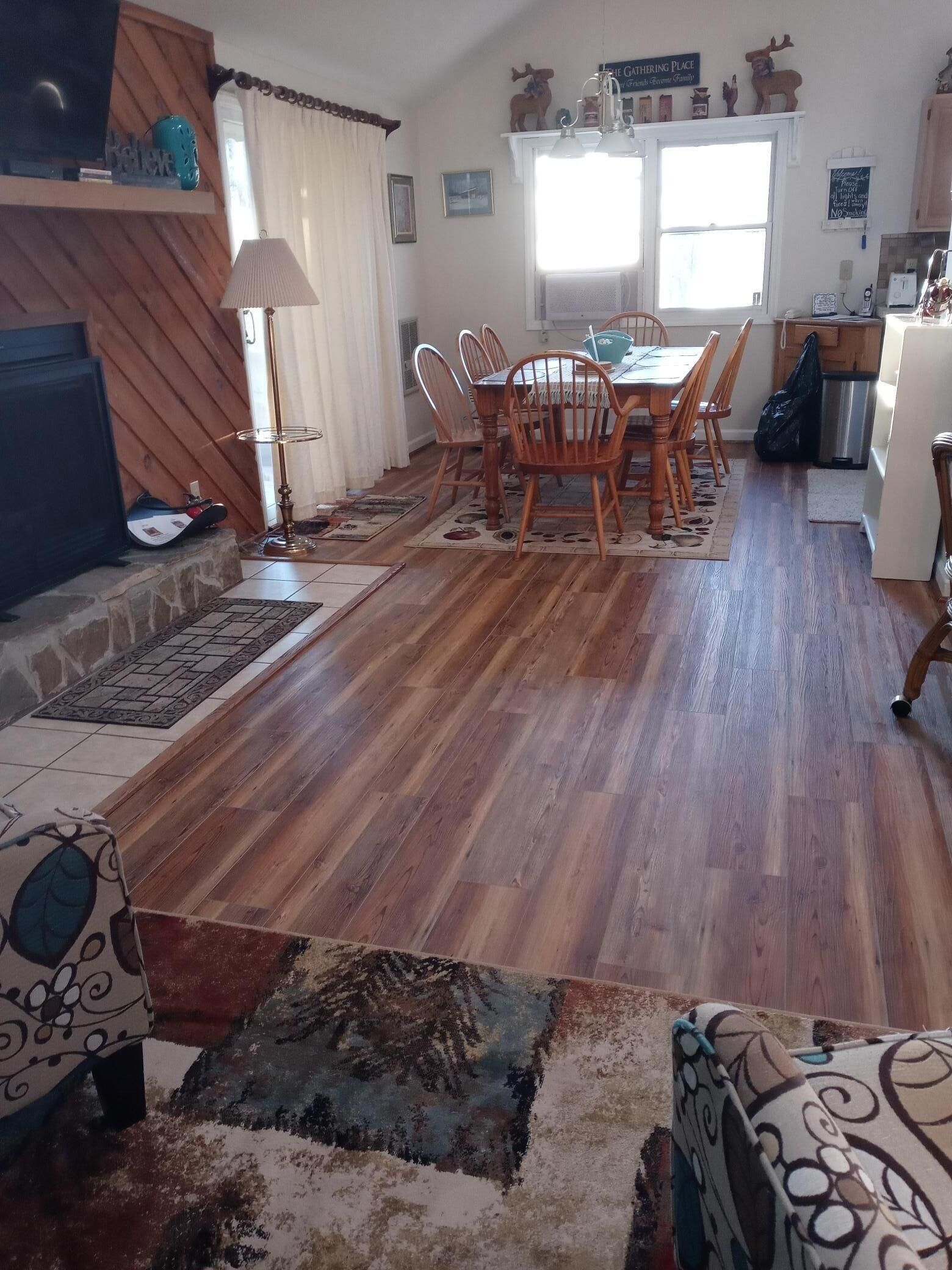 A dining area with wooden flooring, a table with chairs, and a kitchen area in the background.