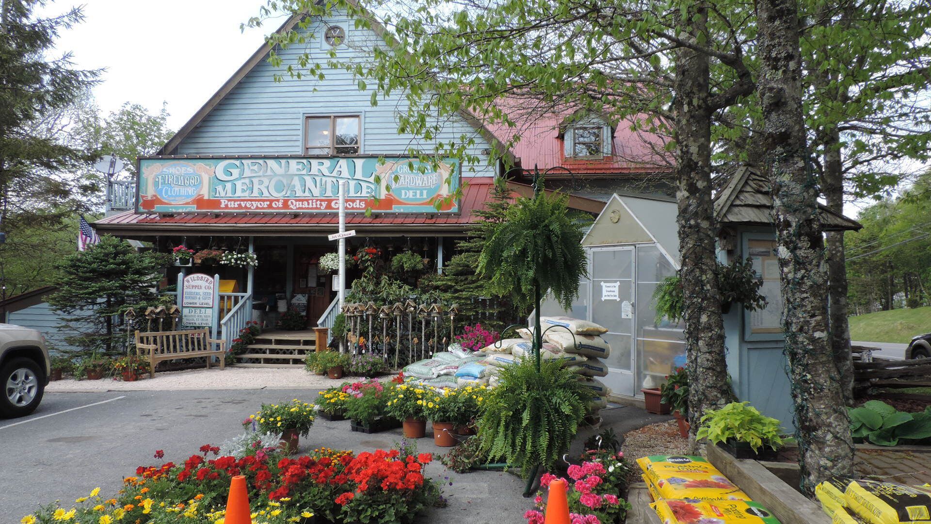 Un bâtiment sur lequel on peut lire l’inscription « Épicerie générale et produits fins », avec une boutique de fleurs devant.