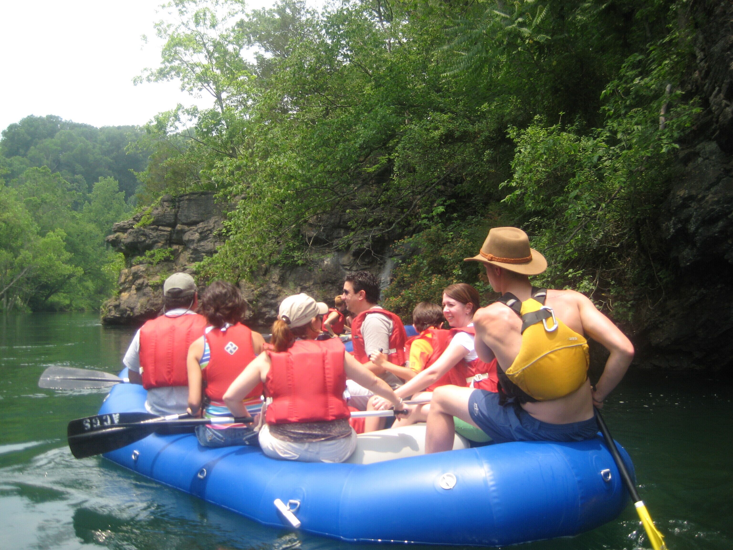 A group of people in a blue raft on a river surrounded by greenery.