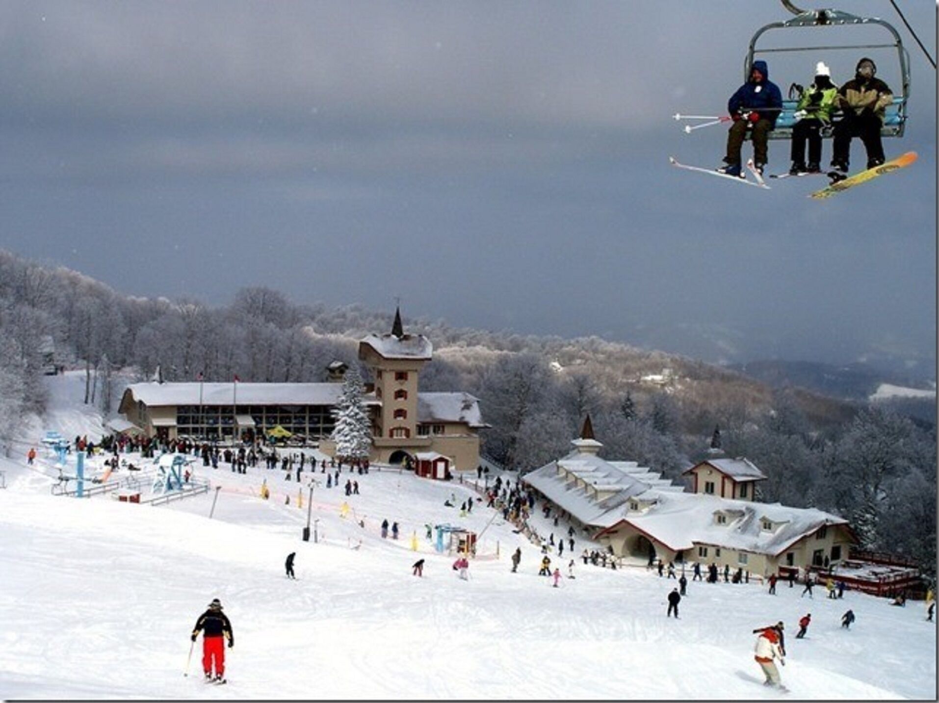A ski resort with multiple buildings, including a large lodge and a tower, surrounded by snow-covered trees.