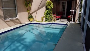 A rectangular pool with a blue tile edge, surrounded by a concrete deck. There are potted plants and a red chair visible. - Conveniently Located Pool Home w/ Free WiFi & Vaulted ceiling (Tampa)