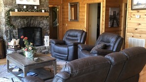 L’intérieur d’un chalet chaleureux, avec une cheminée en pierre, des canapés en cuir et une tête de cerf accrochée au mur.
