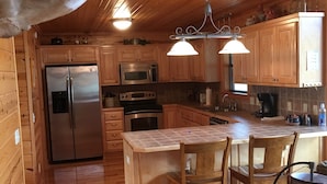L’intérieur d’une cabane en bois comprend une cuisine équipée d’un réfrigérateur, d’un four à micro-ondes, d’une cuisinière et d’armoires en bois.
