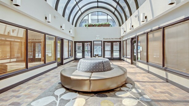A spacious atrium with a central seating area, large windows, and a sign indicating a plaza and ski area. - Studio Premier Condo | Ski-in/Skit-out Access (Breckenridge)