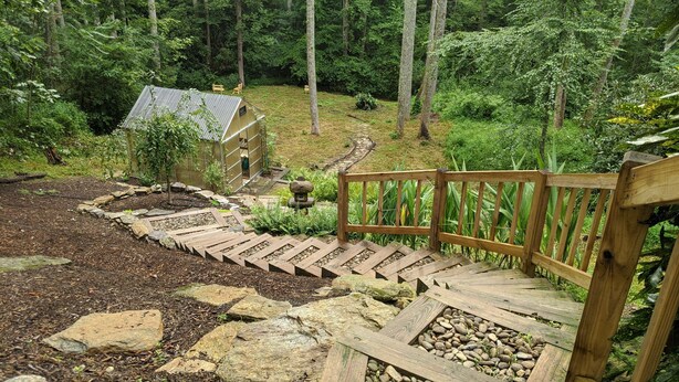 Una escalera de madera que conduce a una casa rodeada de un jardín con un sendero de piedra y una valla de madera.