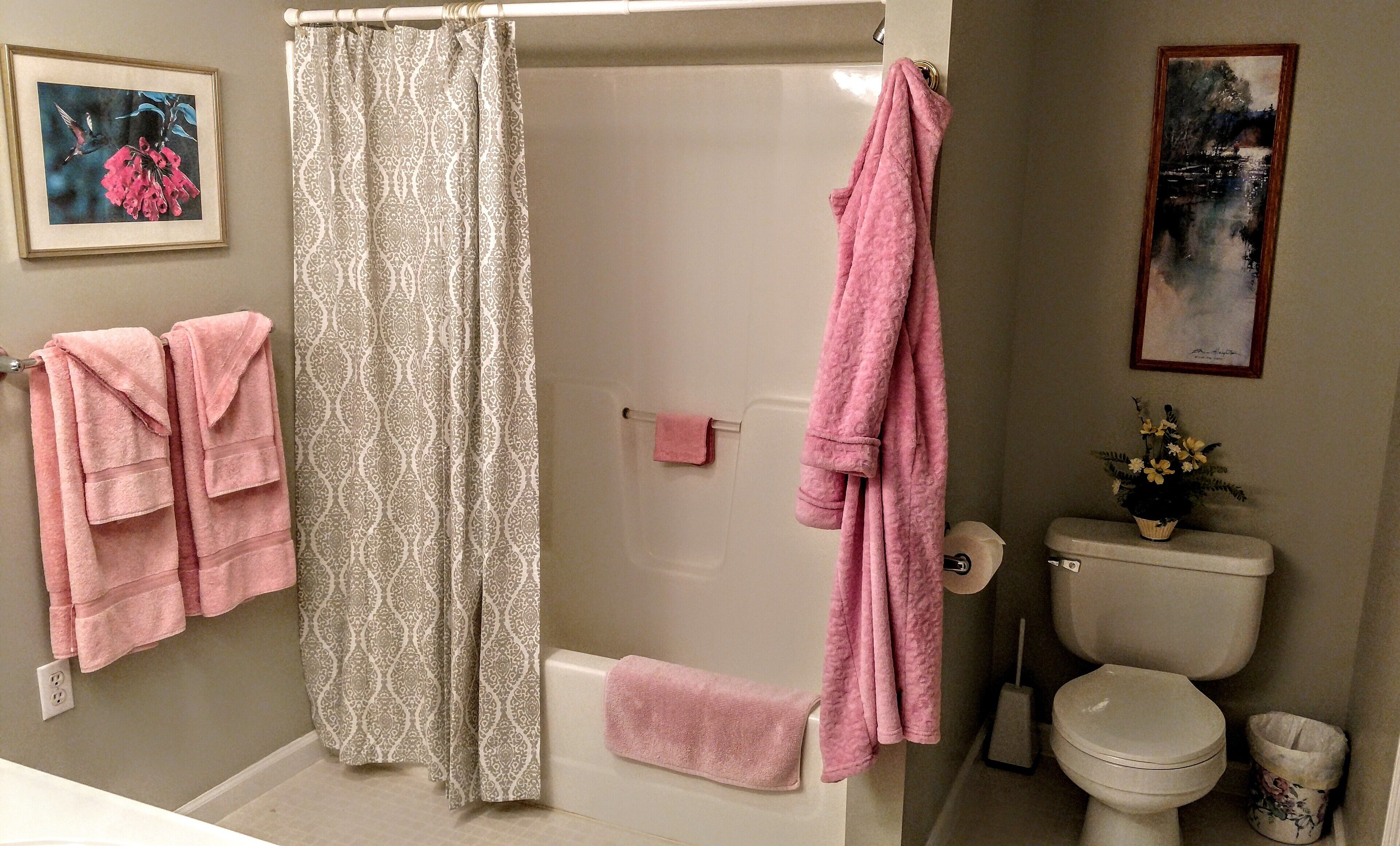 A bathroom with a shower curtain, a toilet, a sink, and a framed painting on the wall.