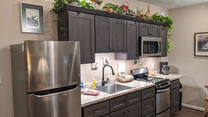Una cocina con armarios oscuros, un refrigerador de acero inoxidable, un microondas, una estufa a gas y un lavamanos.