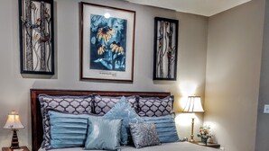 Un dormitorio con una cama grande, dos mesitas de noche y una lámpara de noche, además de detalles decorativos en la pared.