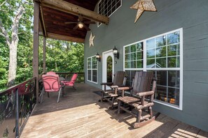 A covered deck with wooden chairs and a red chair, large windows, and a wooden ceiling fan. - Cloud 9 Cabin with an indoor pool, hot tub, & fire pit! (Bryant)