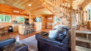 A wooden cabin interior with a living area, kitchen, and a staircase.