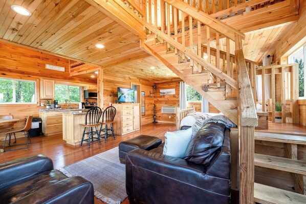 Interno di una baita in legno con angolo living, cucina e una scala.