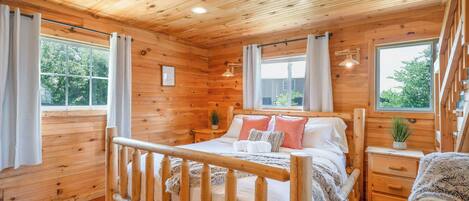 A wooden cabin bedroom with a bed, bedside tables, and windows.