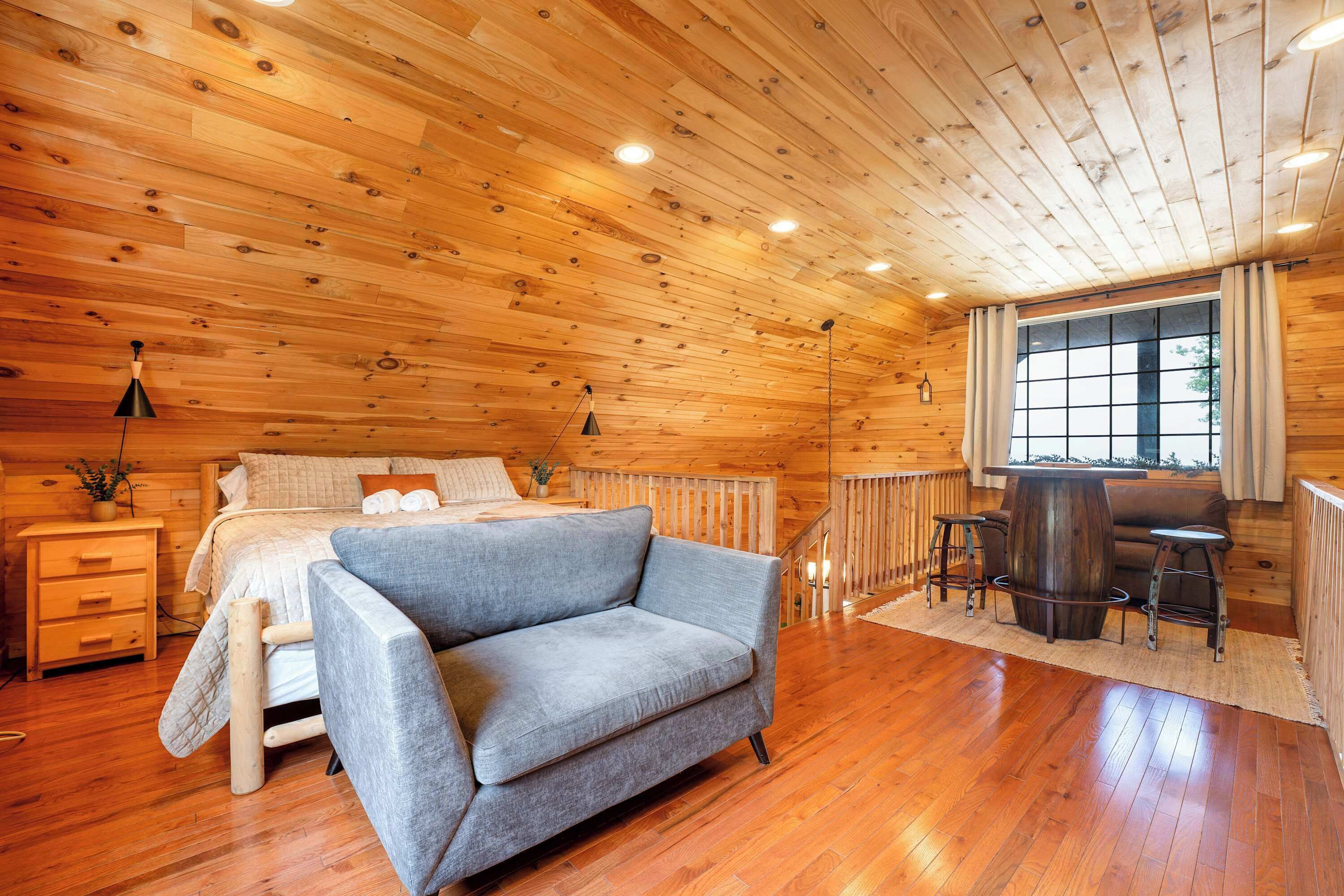 L’intérieur d’un chalet en bois comprend un lit, un canapé gris, un plancher en bois et un coin repas avec une table et des chaises.