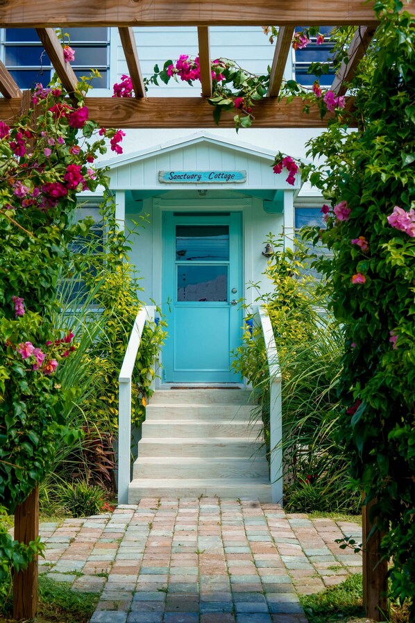 A cottage with a turquoise door and a sign reading "Sanctuary Cottage."