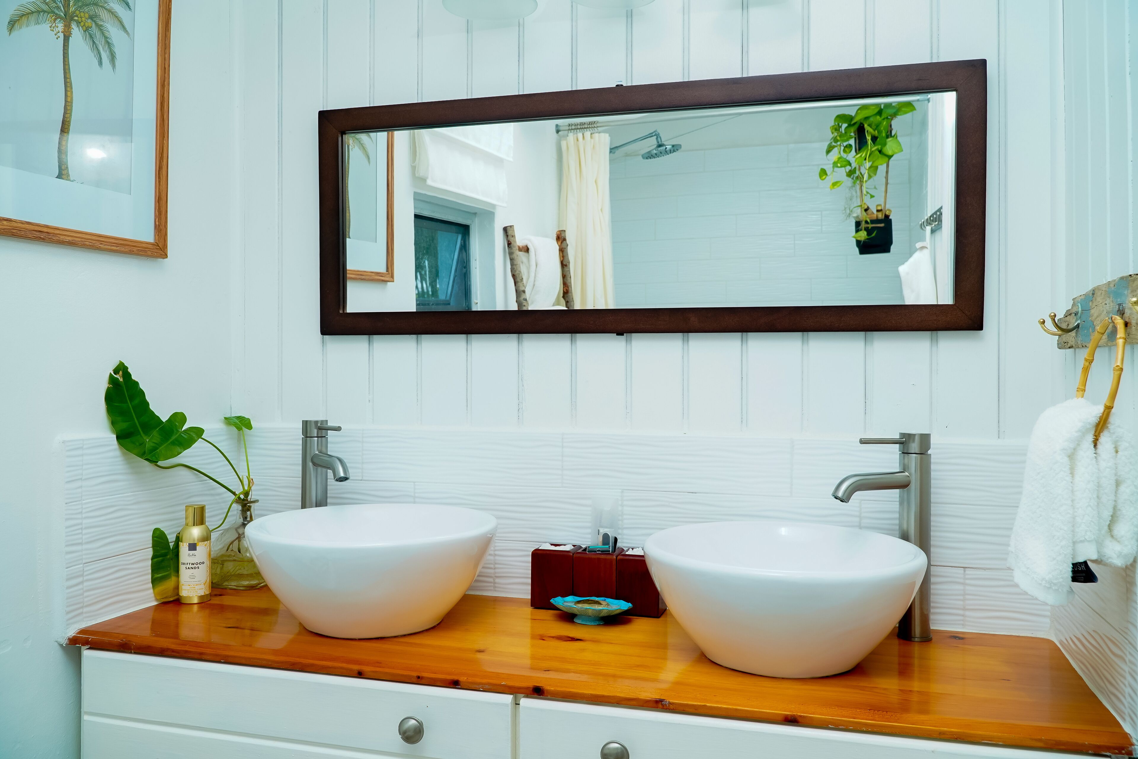 Een badkamer met twee witte wastafels, een houten wastafelmeubel, een grote spiegel en een kamerplant.