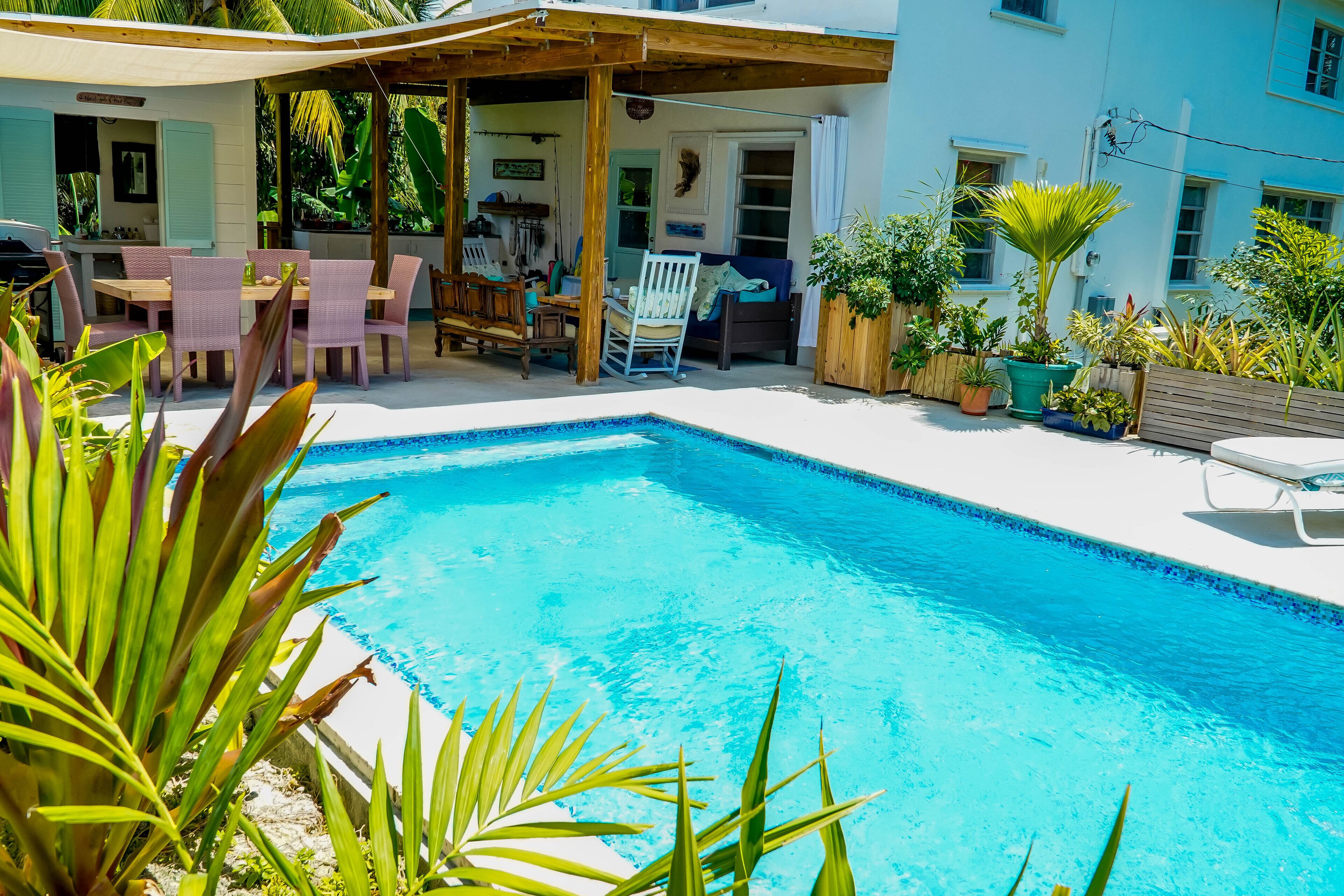 A pool area with a wooden deck, lounge chairs, and potted plants.