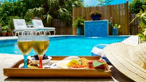 A poolside setting with lounge chairs, a tray with drinks and snacks, and a wooden fence in the background. - The ONLY house with POOL for rent in Spanish Wells! Five star service. (Spanish Wells)