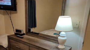 A wooden dresser with drawers, a mirror, a lamp, and a television mounted on the wall.