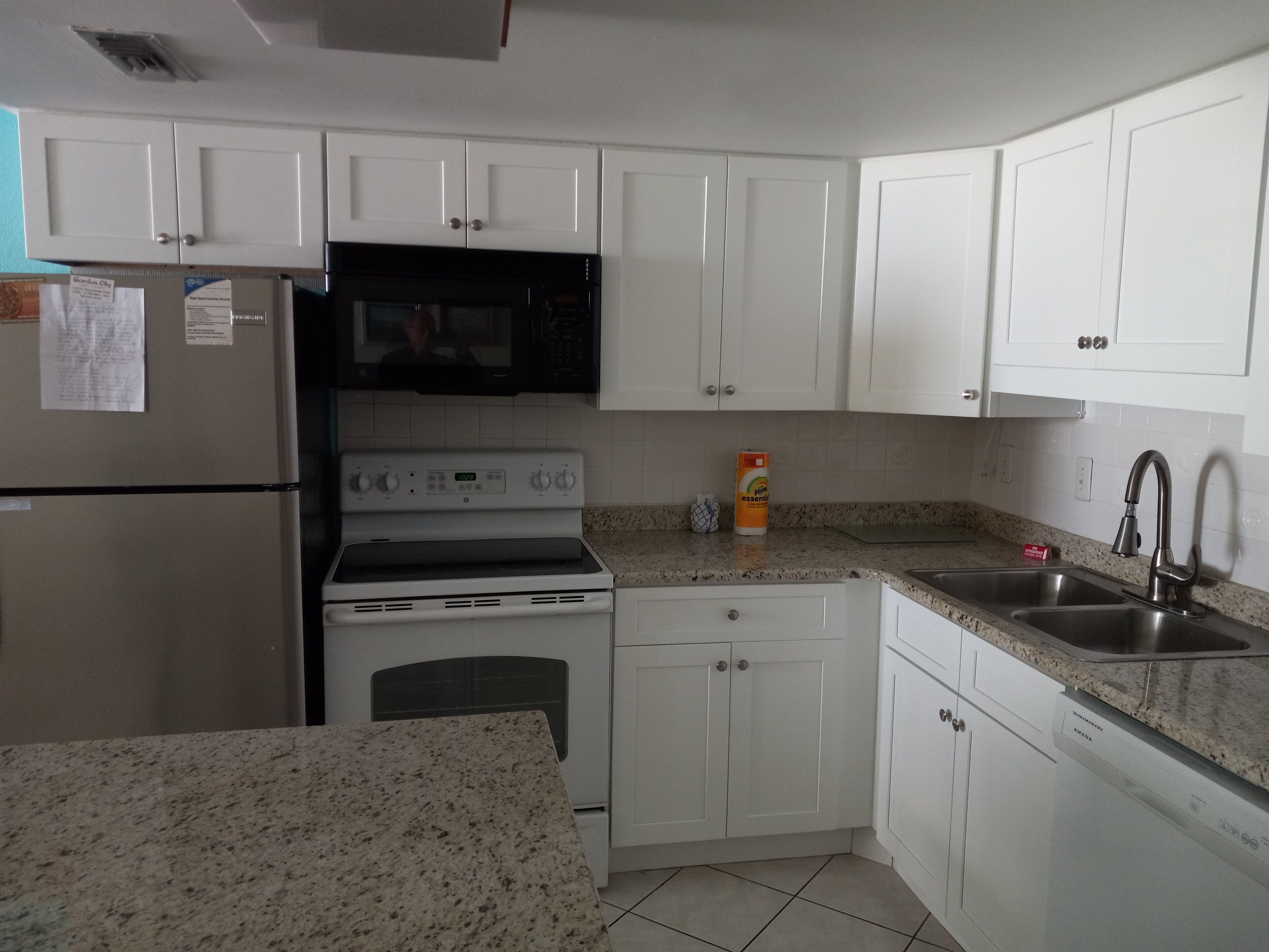 A kitchen with white cabinets, a stainless steel refrigerator, a microwave, an oven, a dishwasher, and a granite countertop.