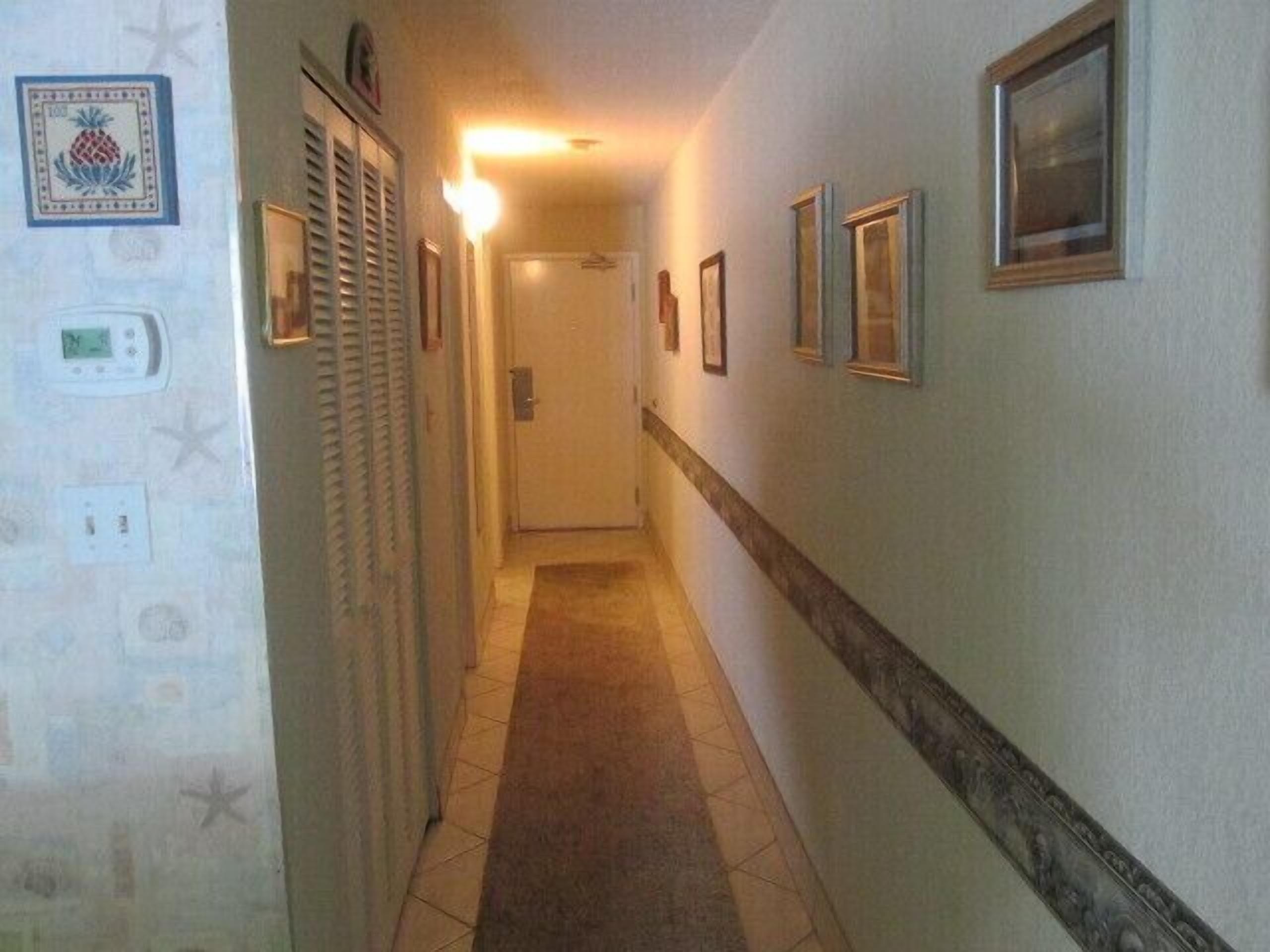 A narrow hallway with a carpeted floor, a door at the end, and framed pictures on the walls.