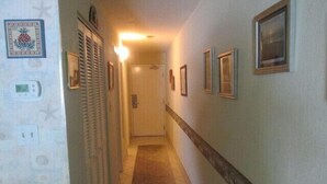 A narrow hallway with a carpeted floor, a door at the end, and framed pictures on the walls.