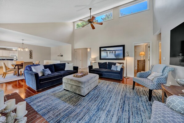 A spacious living room with a large TV, comfortable seating, and a ceiling fan.